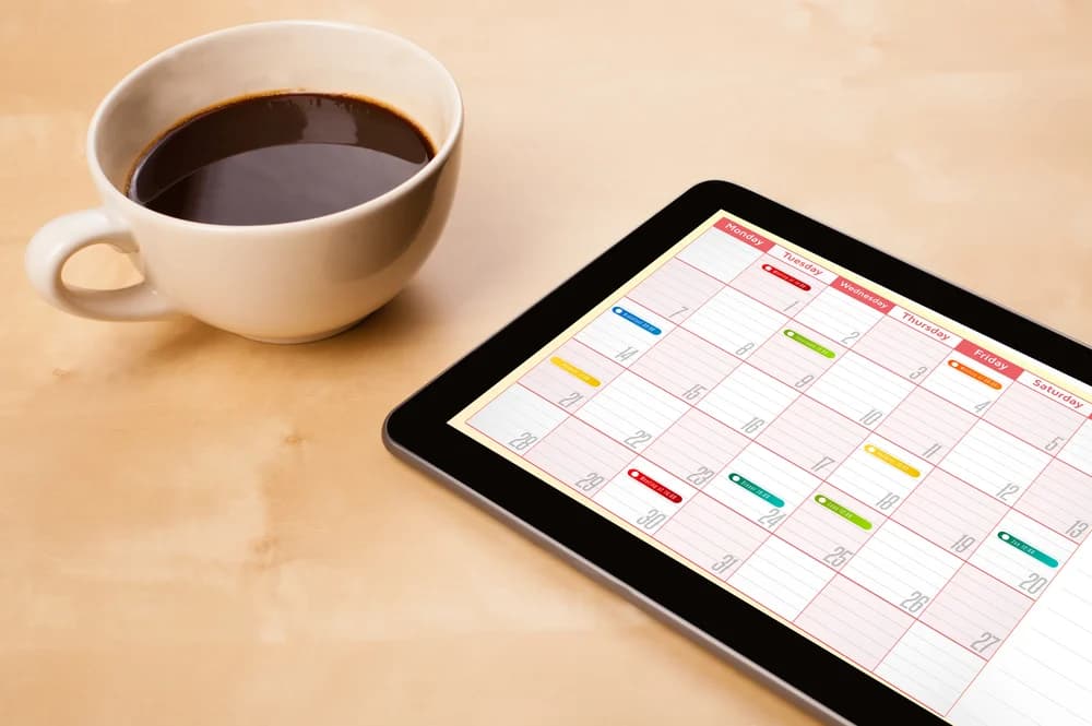 Calendar displayed on a tablet beside a cup of coffee.