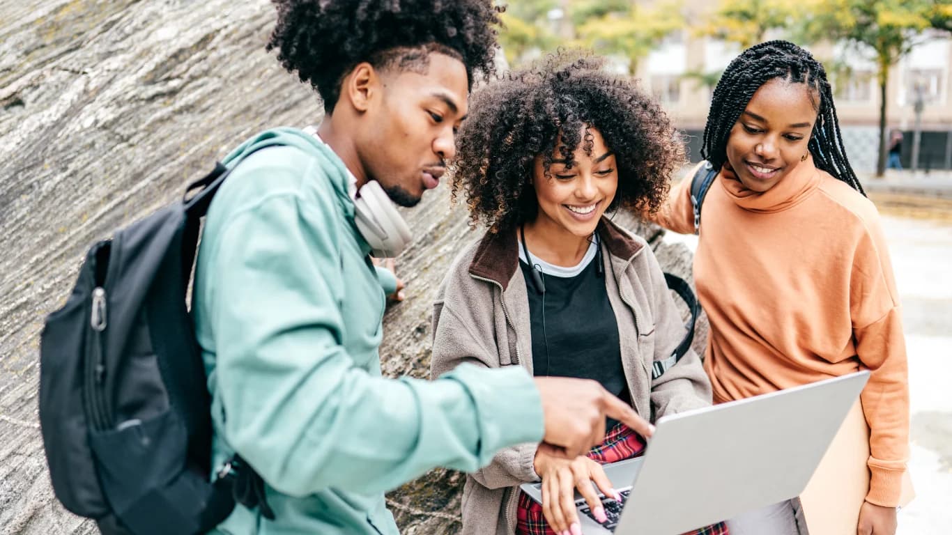 Three students looking at a laptop together outdoors.