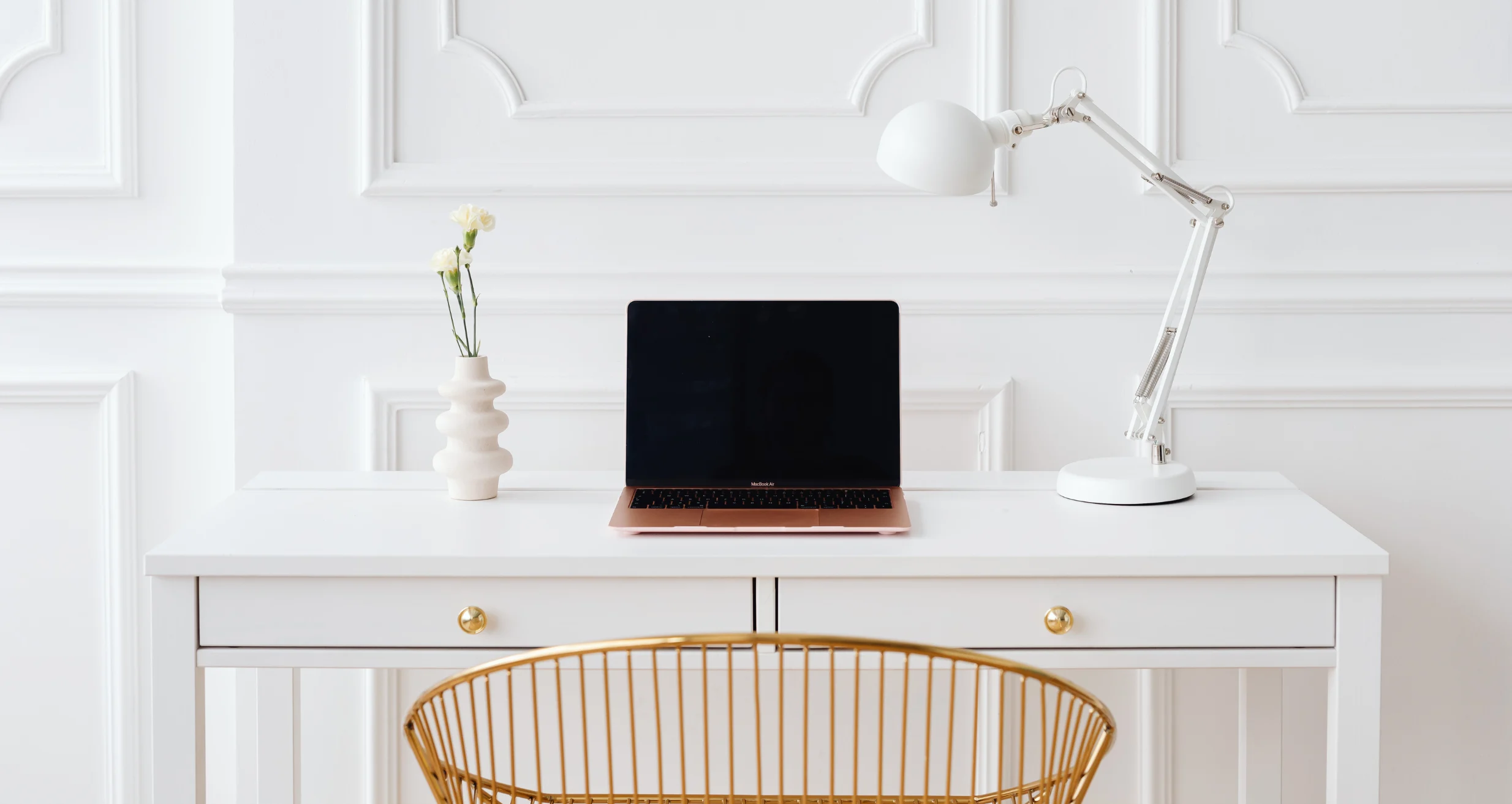 White desk with a laptop, lamp, and plant.